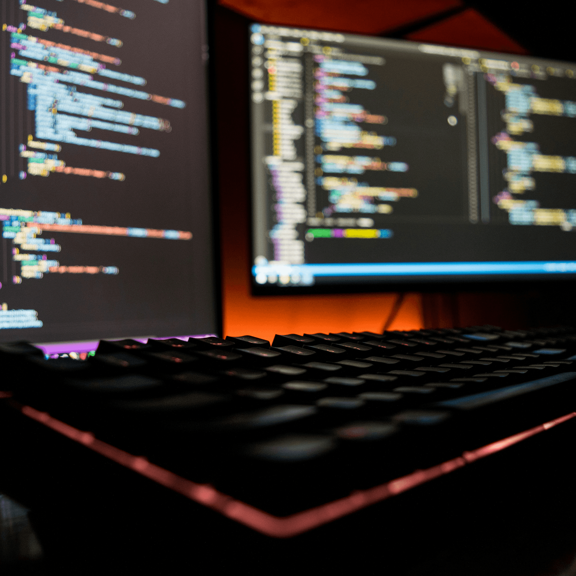 Two monitors displaying code beside a keyboard in a dark workspace.