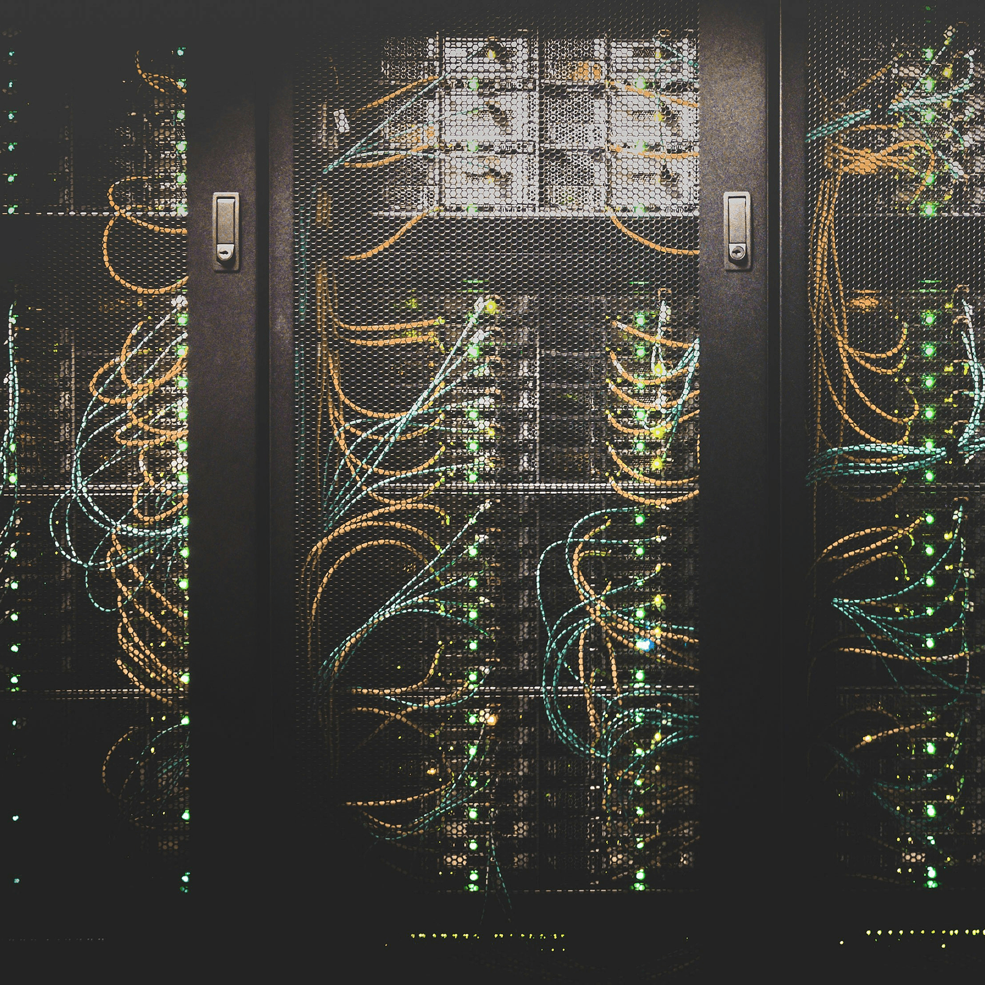A photograph of server racks behind mesh cabinet doors, with network cables and green status lights visible in a dark data centre.